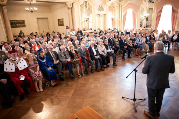 Liczna grupa osób – uczestnicy zjazdu siedzą na krzesłach, przed nimi stoi mężczyzna przy mikrofonie