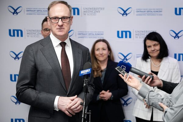 Mężczyzna stoi przy mikrofonie udzielając wywiadu, dwie kobiety stoją za nim