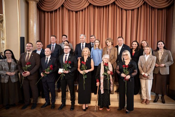 Grupa mężczyzn i kobiet pozuje do zdjęcia, osoby w pierwszym rzędzie trzymają kwiaty, legitymacje i odznaczenia