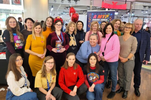 Grupa kilkunastu osób stoi i klęczy w centrum handlowym przy stoisku 34. Finału WOŚP