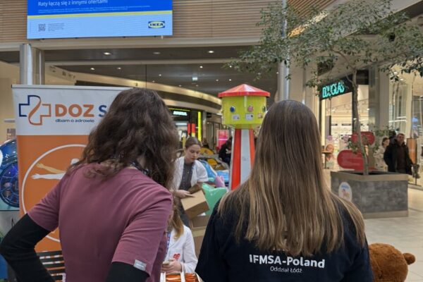 Dwie osoby stoją tyłem przy stole informacyjnym